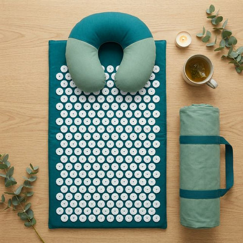 Flat-lay of acupressure mat set with pillow, carry bag, tea, and eucalyptus on oak surface
